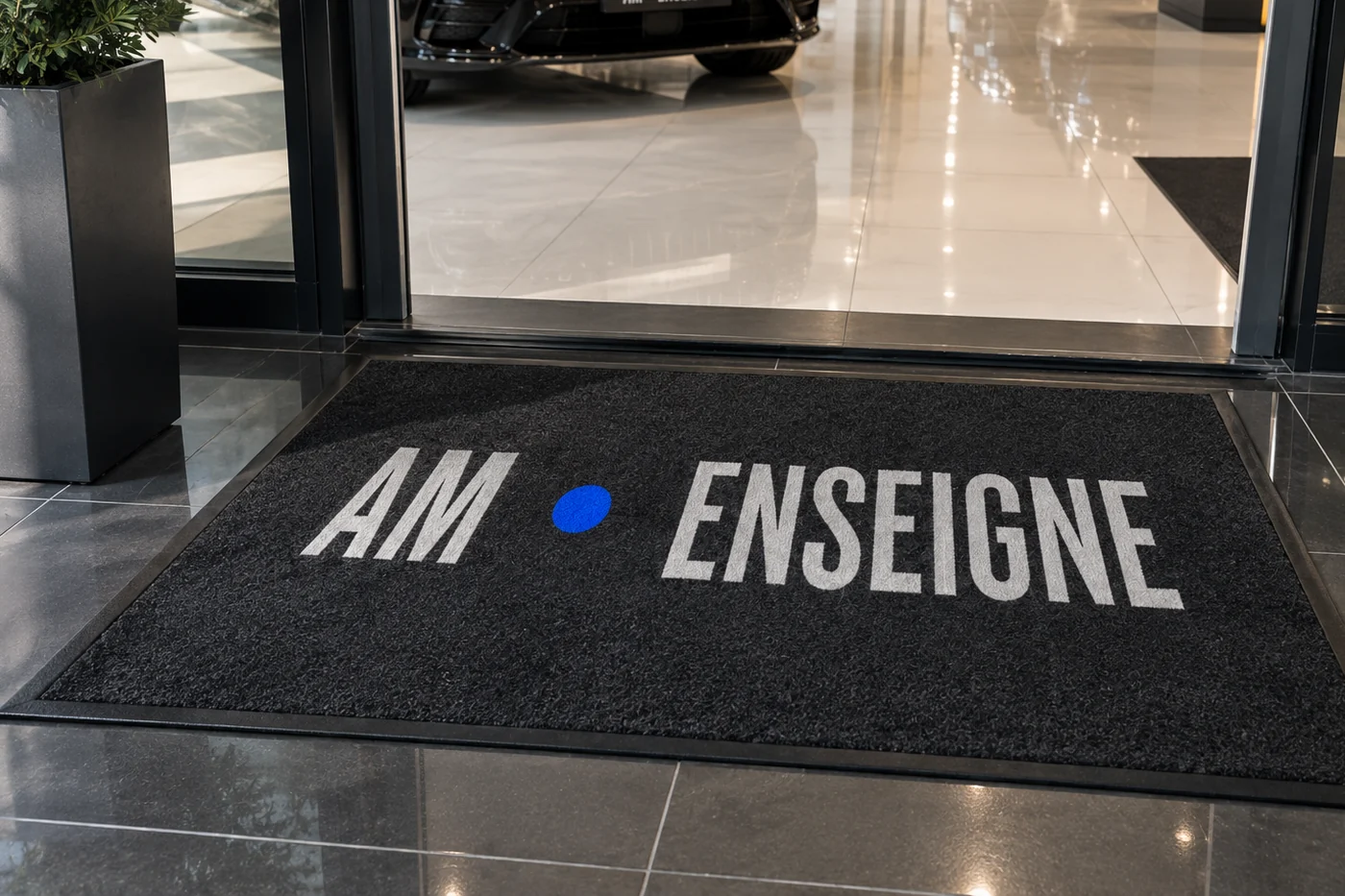 Tapis d’entrée personnalisé, logo AM - ENSEIGNE imprimé, posé dans le sas vitré d’une concession automobile